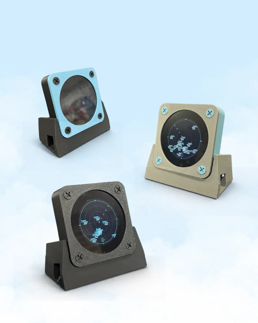 Three printed flight radar units in blue, tan and black, on angled stands. The screens show a radar scope with range rings and labelled aircraft.